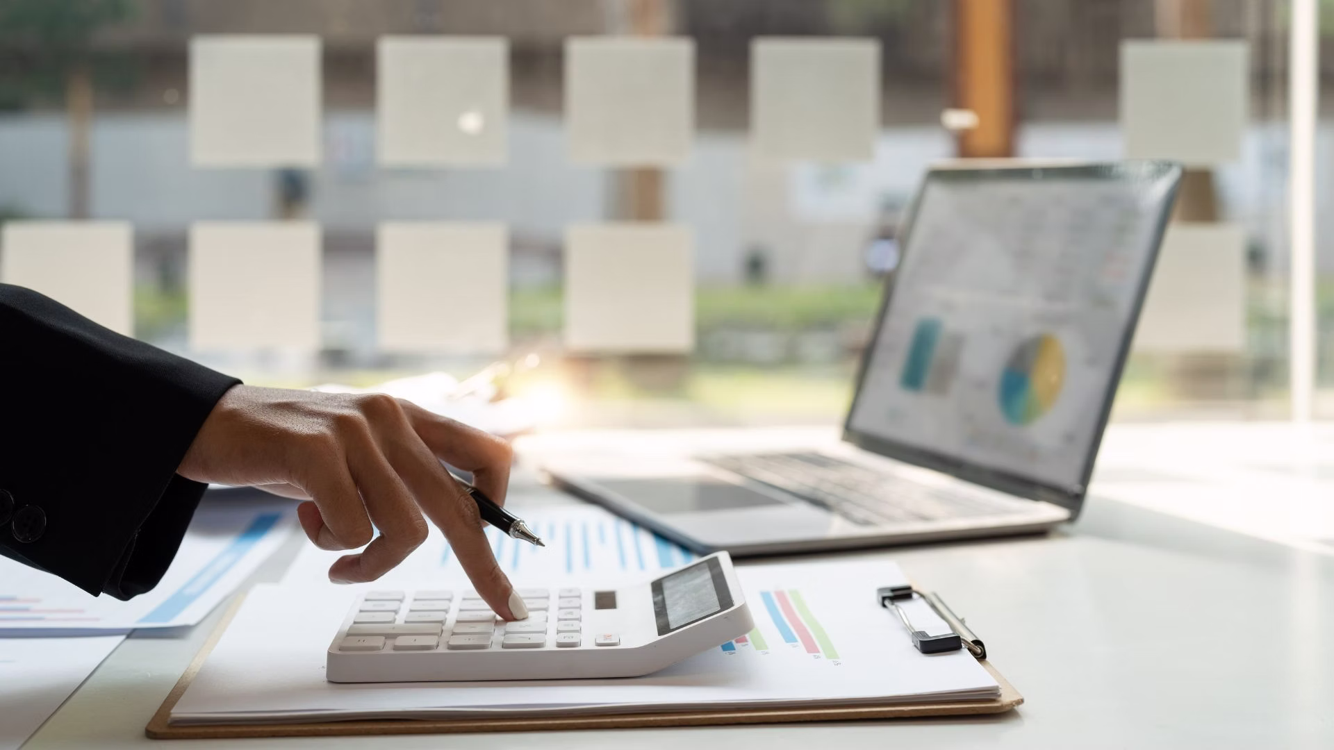 Osoba licząca koszty firmy przy biurku z laptopem i kalkulatorem – wirtualne biuro w Łodzi.